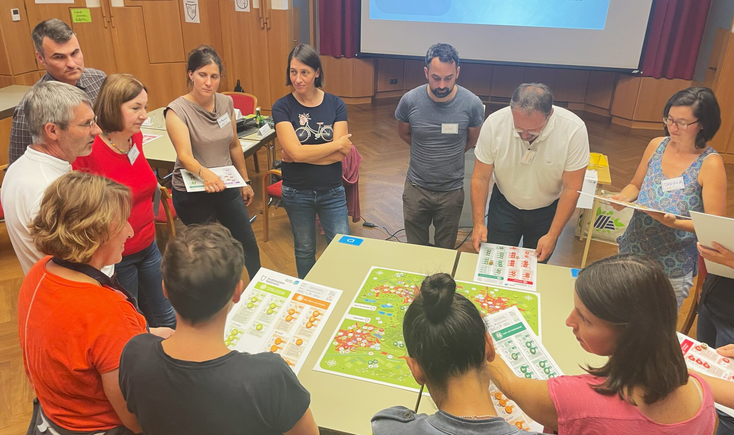 Zu sehen sind Menschen, die im Zuge des Klimaplanspiels in Frohnleiten um einen Spieltisch stehen und disuktieren.