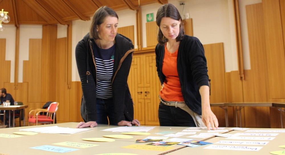 Zwei Vertreterinnen der Klimadialog-Pilotgemeinden stehen an einem Tisch.